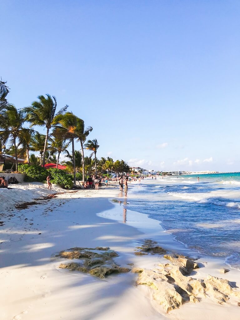 looking north along Playacar beach in Playa del Carmen as tourists and locals lounge in the sand and the water.