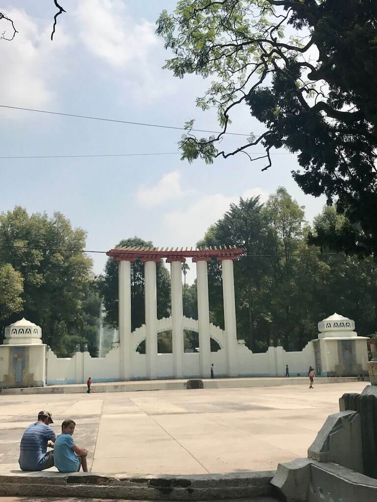 a boy and his day sit in front of a monument at parque españa, mexico city