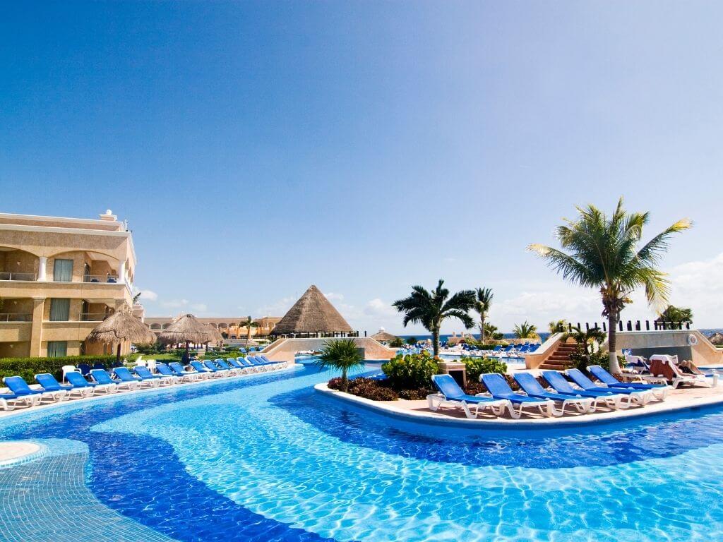 blue lounge chairs lined up along the edge of a sparkling swimming pool at an all inclusive hotel in playa del carmen